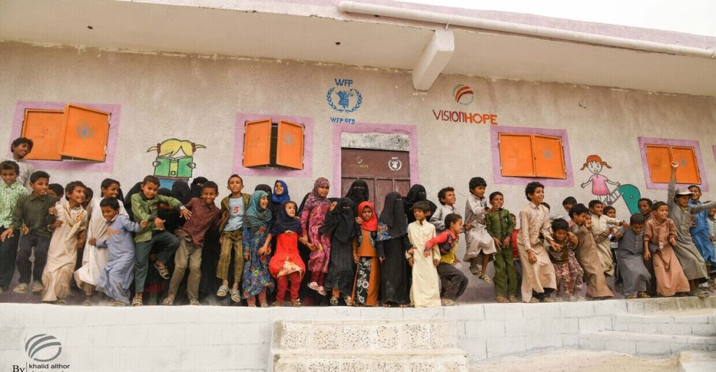 Smiling children playing outside a colorful school supported by the World Food Programme and Vision Hope.