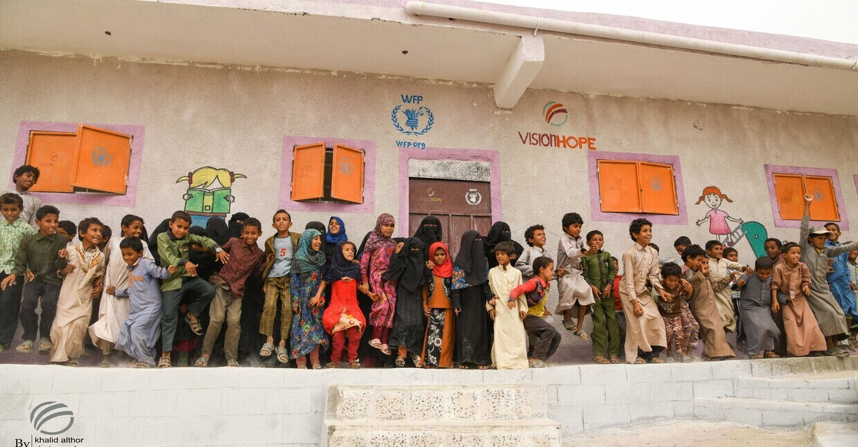 Smiling children playing outside a colorful school supported by the World Food Programme and Vision Hope.
