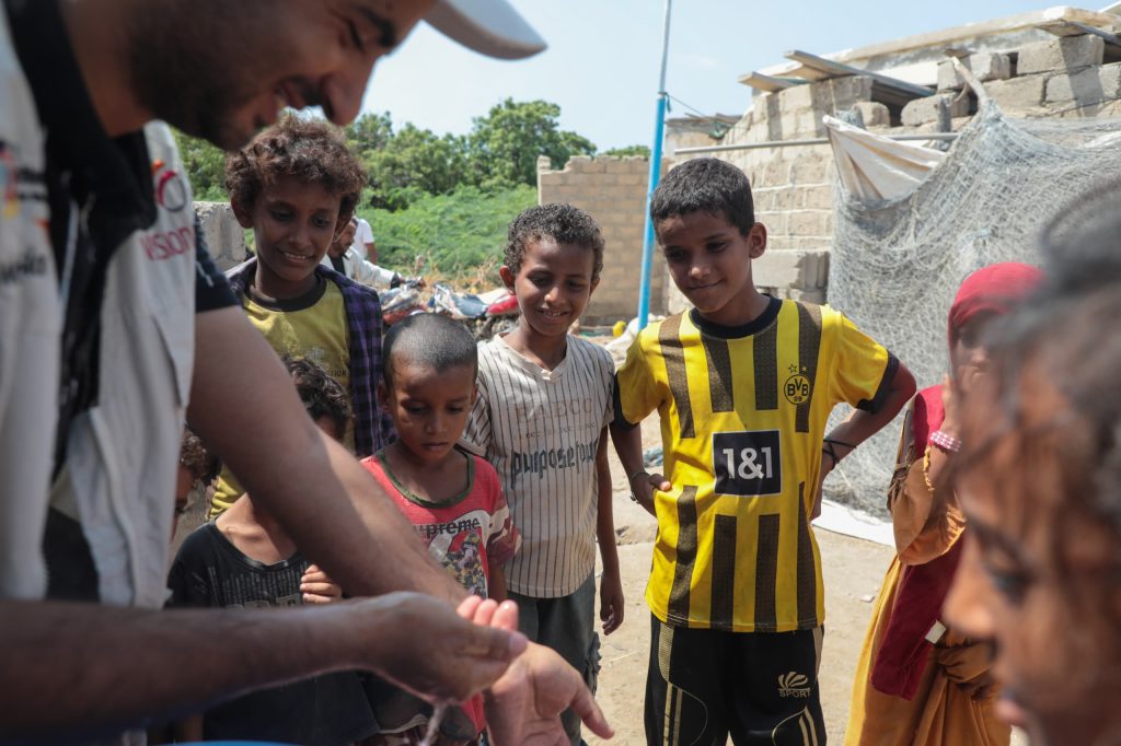 Technician repairing a community water tap while children wait to collect water in Yemen