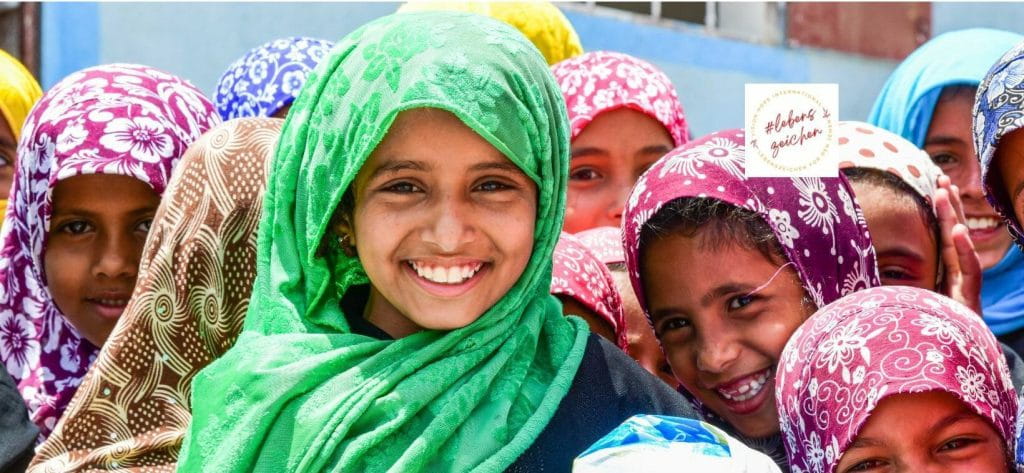 Smiling Yemeni girls wearing colorful headscarves looking into the camera