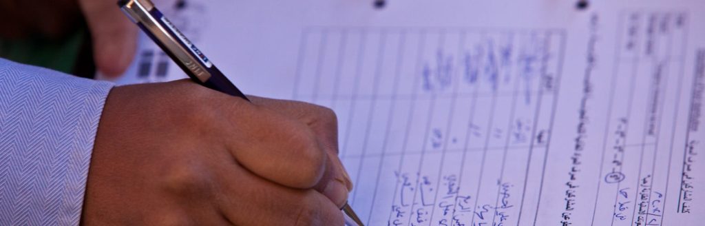 A hand writing data into a structured Arabic-language record sheet with a pen