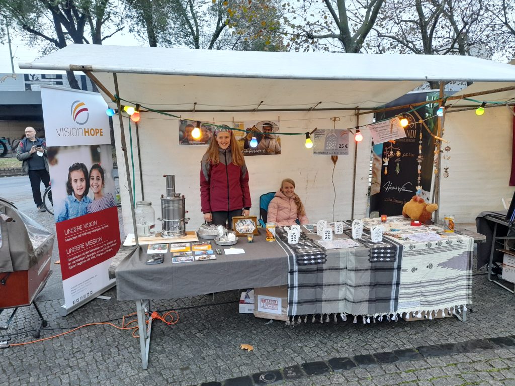 Vision Hope volunteers staffing an information and fundraising stall at a winter market in Germany, with handmade items and project information on display