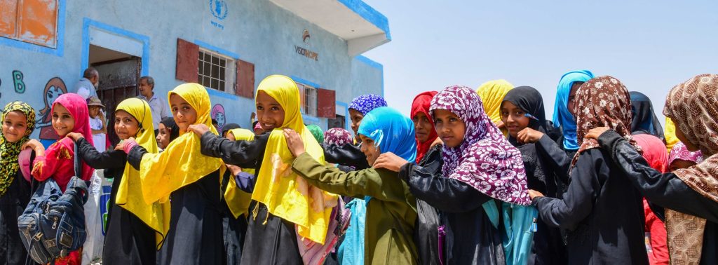 Group of Yemeni schoolgirls in colorful headscarves holding hands in front of their Vision Hope-supported school