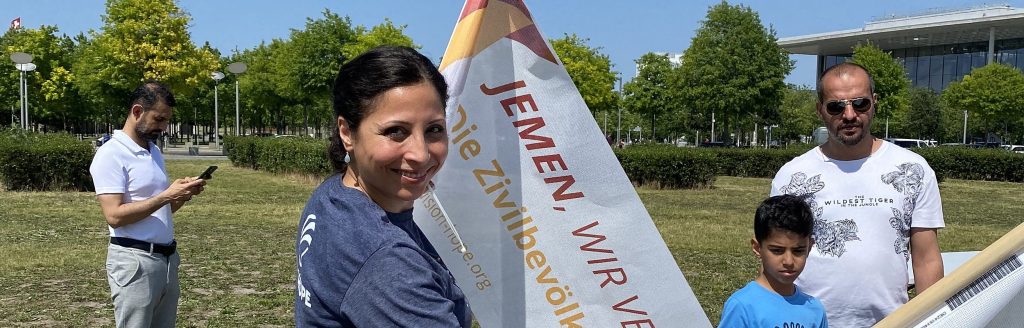 Vision Hope volunteer holding a Yemen campaign flag at an outdoor event in Berlin
