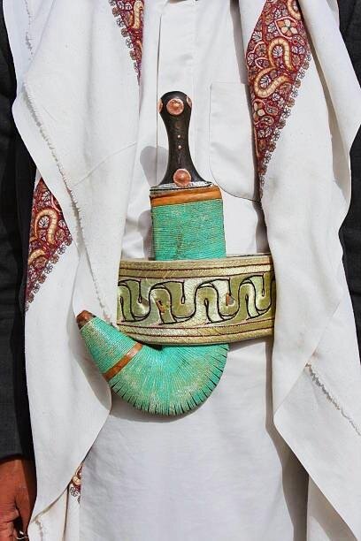 Traditional Yemeni janbiya dagger with turquoise woven hilt worn at the belt over white robes