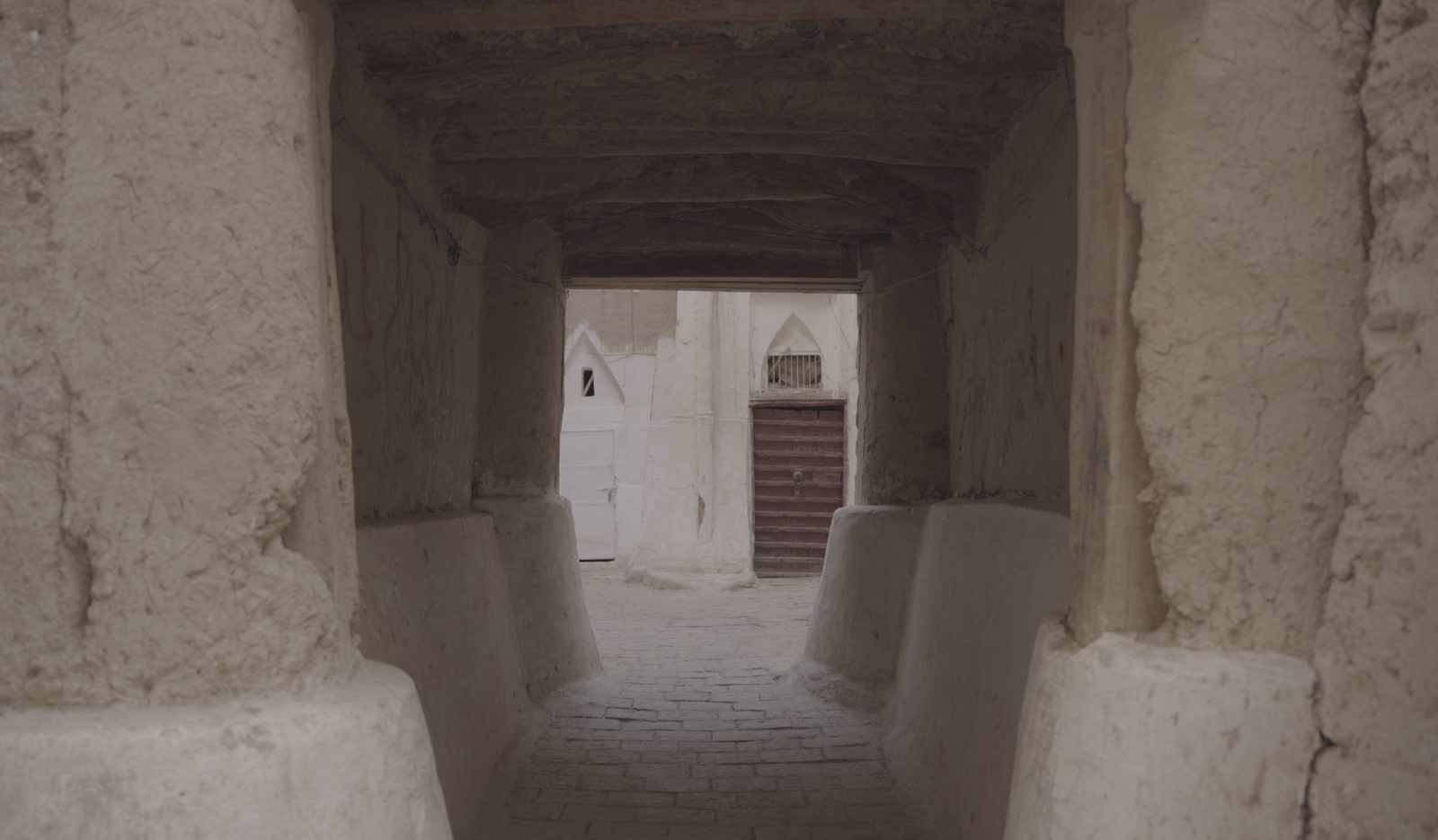Traditional Yemeni mud-brick covered passageway leading to whitewashed old-town buildings and a wooden door