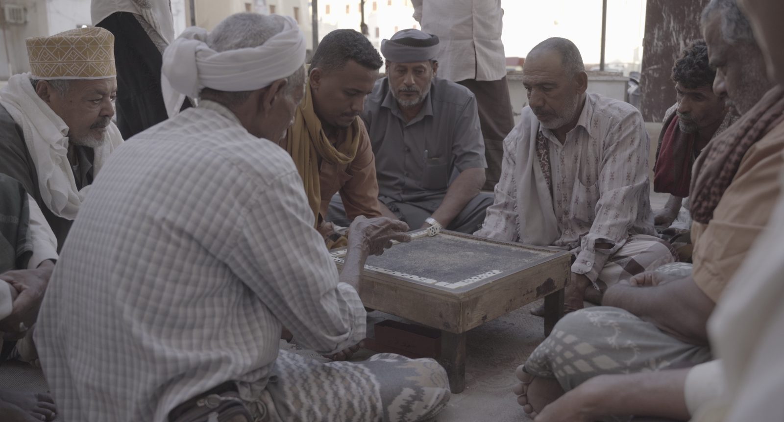 Group of Yemeni men sitting together on the ground playing dominoes, reflecting communal social customs