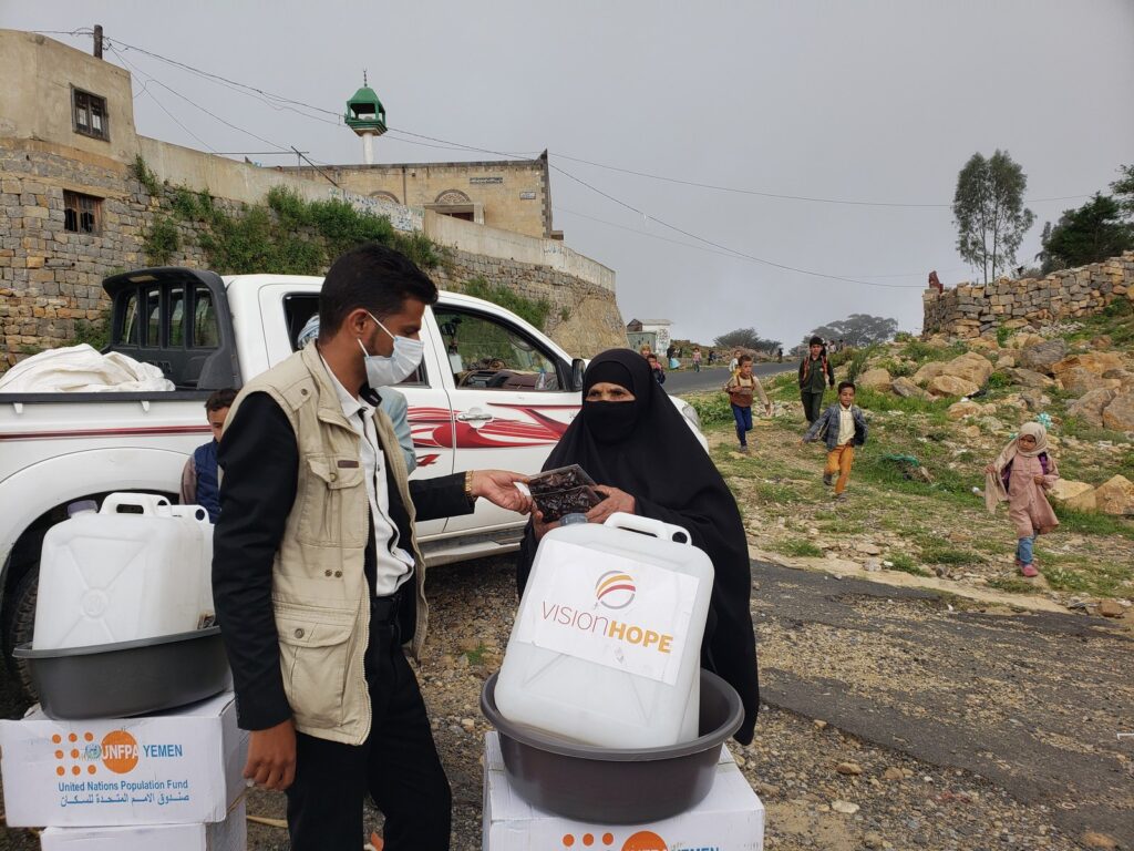 Vision Hope staff hands emergency food rations to a woman beside UNFPA kits in Yemen