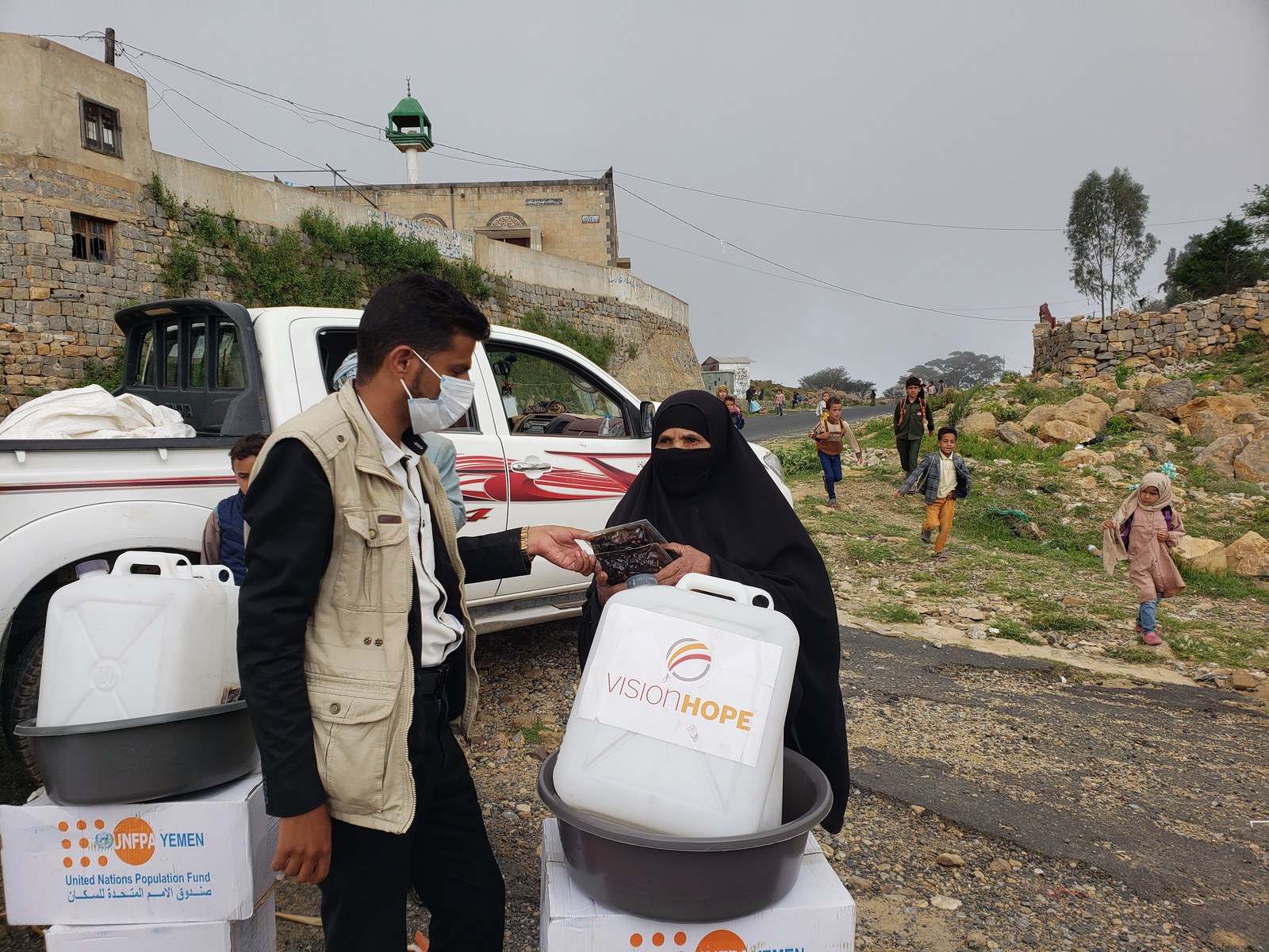 Vision Hope staff hands emergency food rations to a woman beside UNFPA kits in Yemen