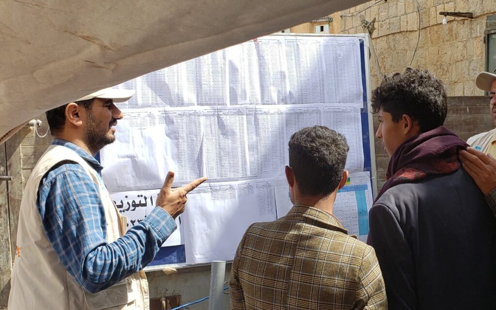 Vision Hope staff member explaining a publicly posted distribution list to men in Yemen